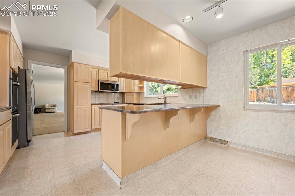 Image 13 of 50: Kitchen with light flooring, a breakfast bar area, light brown cabinets, an