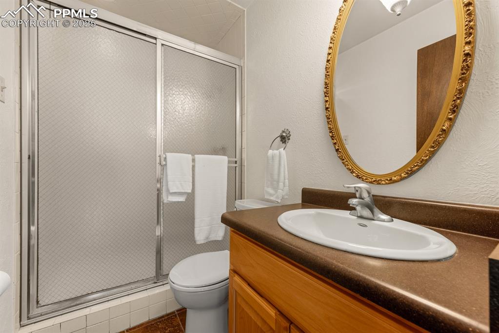 Image 21 of 50: Bathroom with a textured wall, a stall shower, vanity, and dark tile patter