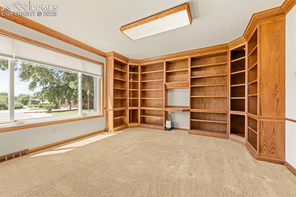 Image 22 of 50: Empty room featuring crown molding, light colored carpet, and built in desk
