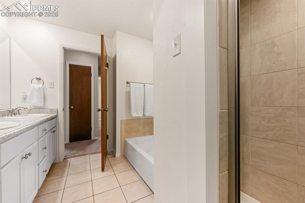 Image 37 of 50: Full bath featuring double vanity, a garden tub, and light tile patterned f