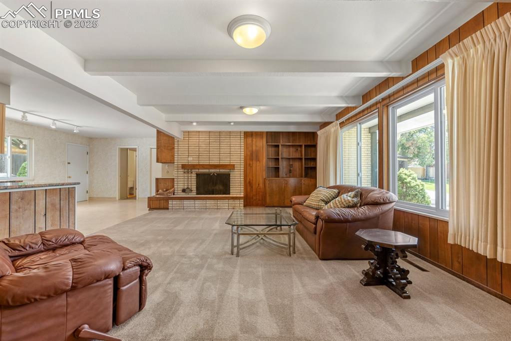 Image 5 of 50: Living room with beamed ceiling, light colored carpet, a brick fireplace, a