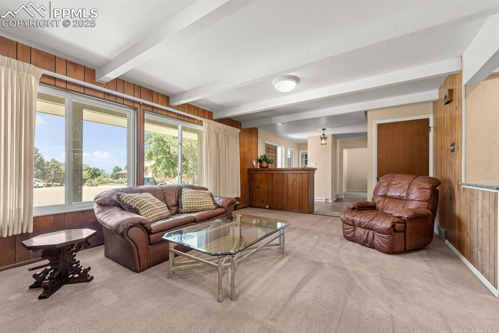 Image 7 of 50: Living area with wooden walls, beamed ceiling, and light carpet