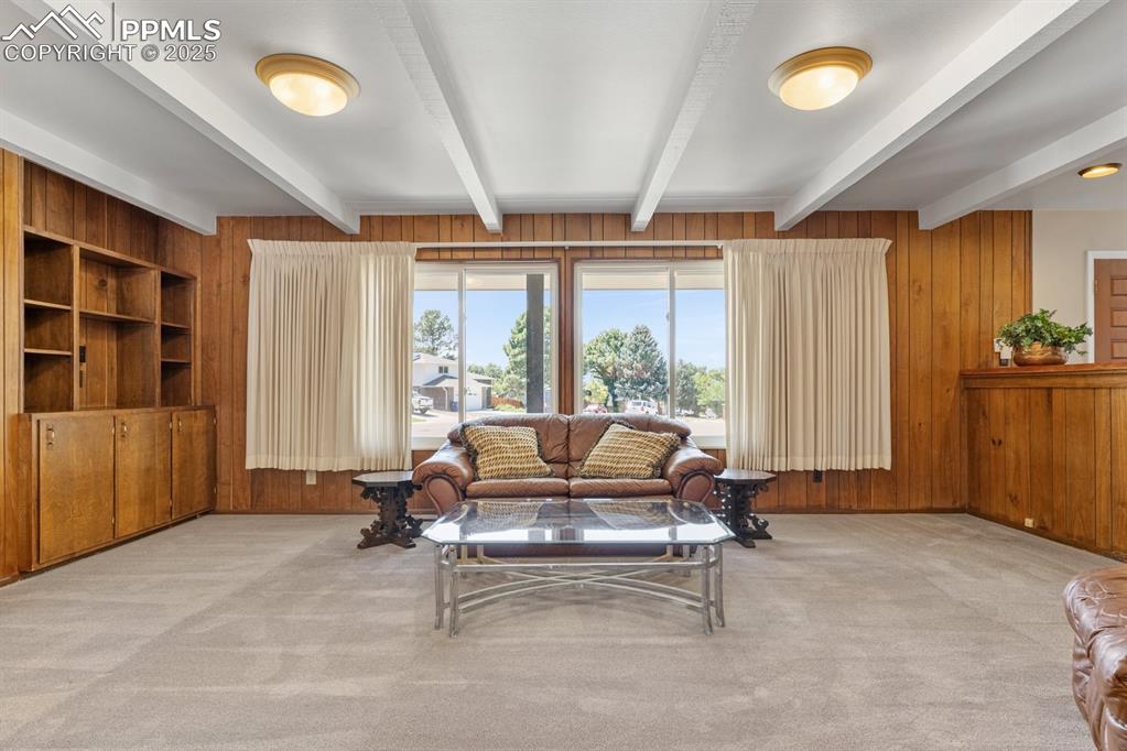 Image 8 of 50: Living room featuring wooden walls, light carpet, and beamed ceiling