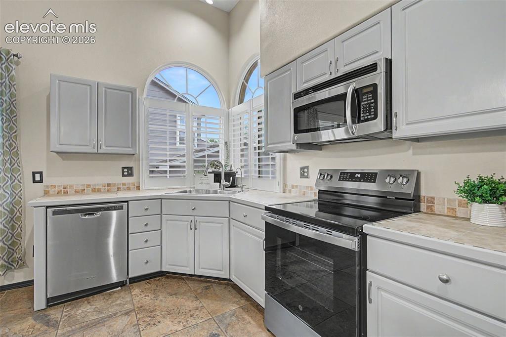 Image 18 of 50: Kitchen featuring stainless steel appliances, light gray cabinetry, and til