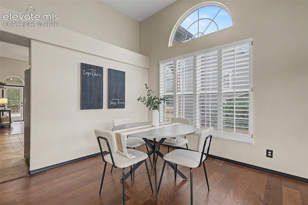 Image 8 of 50: Dining area featuring wood-finish flooring, high ceilings, and a large wind