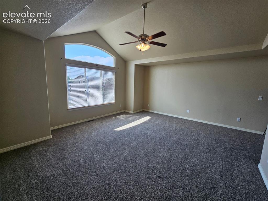 Image 14 of 31: Spacious room featuring vaulted ceilings, a large arched window with blinds