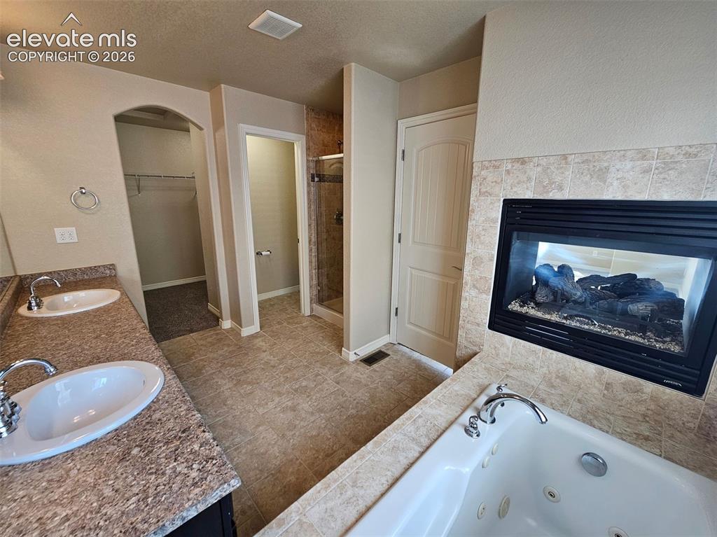 Image 17 of 31: Ceramic tile flooring featuring a built-in fireplace, jetted tub, dual vani