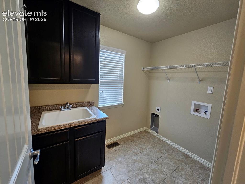 Image 21 of 31: Dedicated laundry room featuring dark cabinetry, a utility sink with a ston