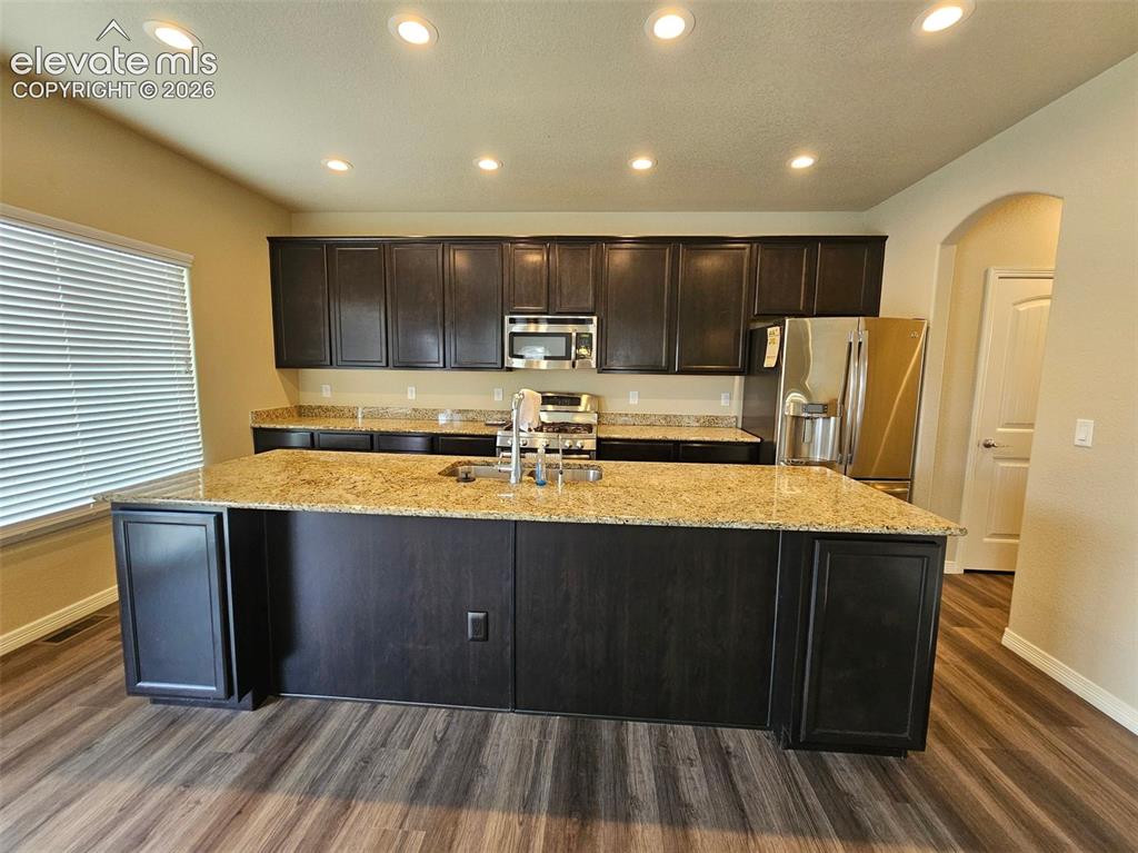 Image 8 of 31: Kitchen featuring wood-finish flooring, dark wood cabinetry, light-toned gr