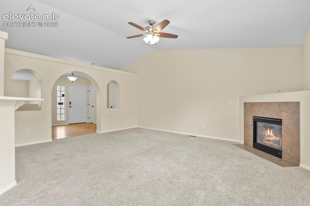 Image 10 of 48: Spacious living area featuring vaulted ceilings, a ceiling fan, plush carpe