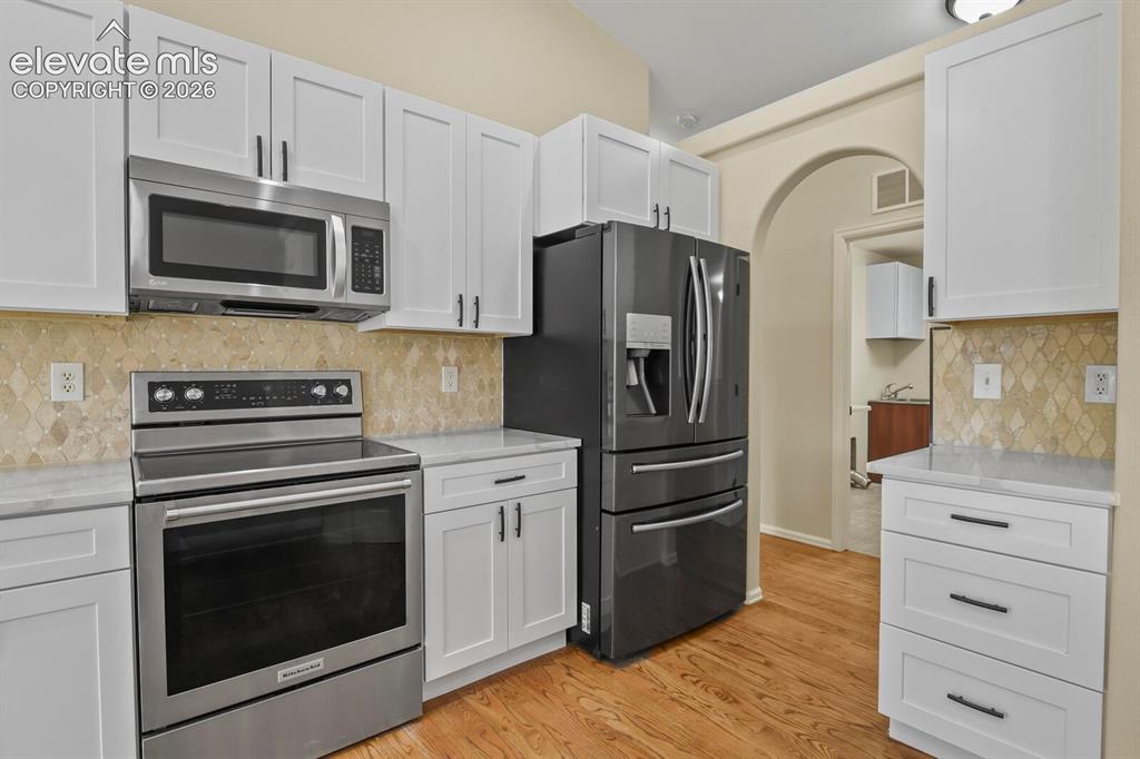 Image 16 of 48: Modern kitchen featuring stainless steel appliances, white cabinetry with d