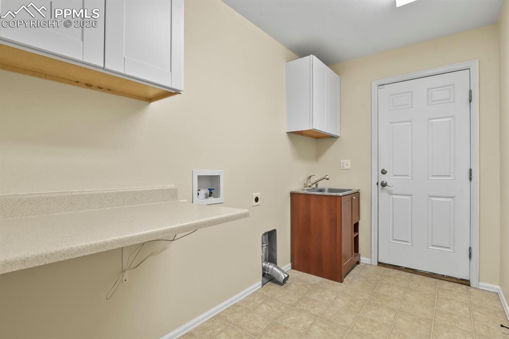 Image 28 of 43: Main level Laundry room featuring a utility sink, white paneled door, tiled