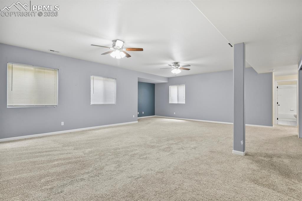Image 29 of 43: Spacious room with light gray walls, plush carpeting, multiple ceiling fans