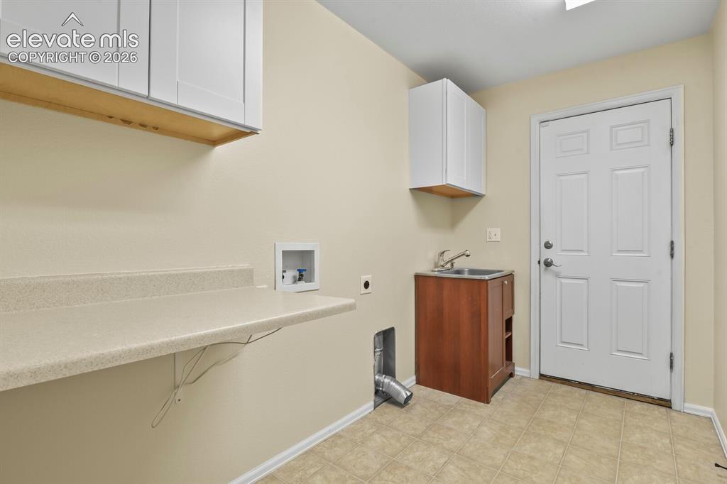 Image 31 of 48: Main level Laundry room featuring a utility sink, white paneled door, tiled