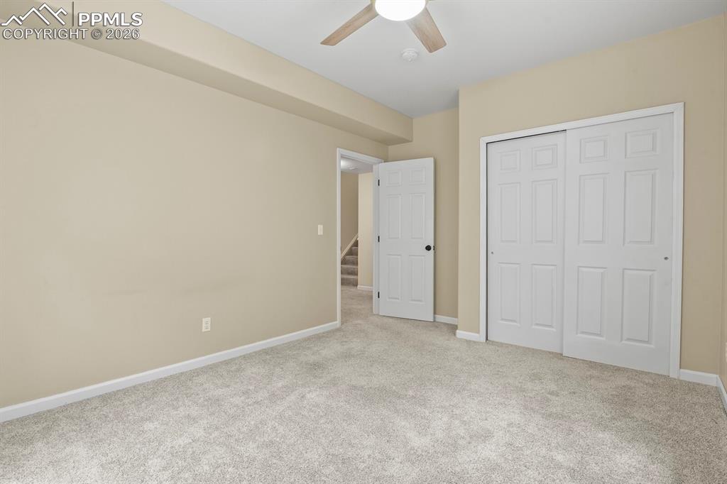 Image 34 of 43: Carpeted room with a ceiling fan, light beige walls, white baseboards, and 