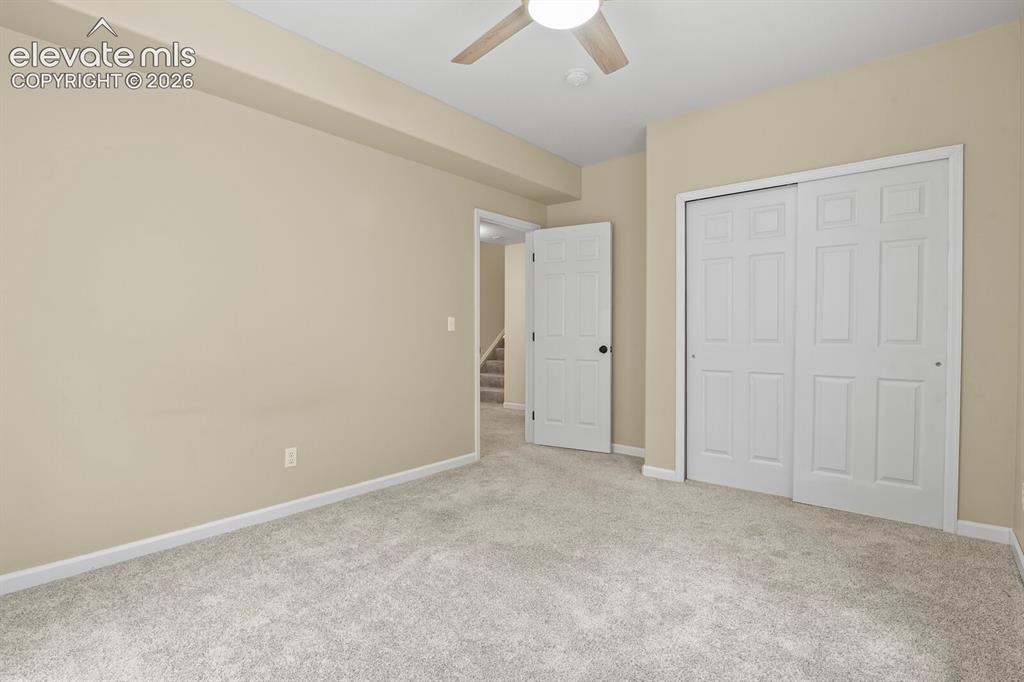Image 38 of 48: Carpeted room with a ceiling fan, light beige walls, white baseboards, and