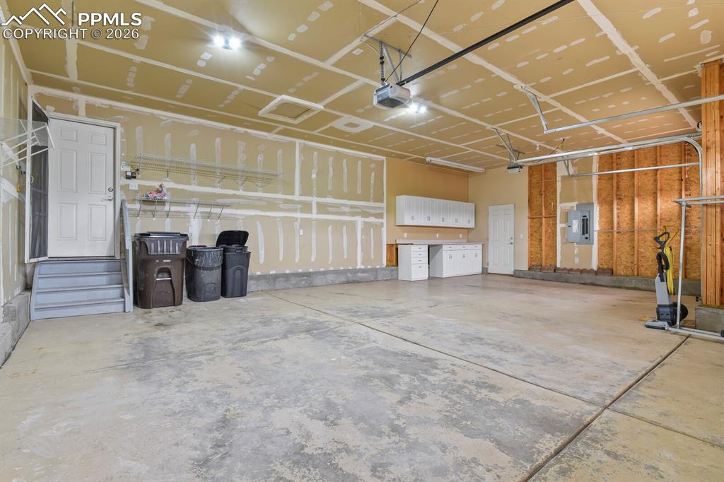 Image 39 of 43: Spacious three-car garage featuring a concrete floor, built-in cabinetry wi