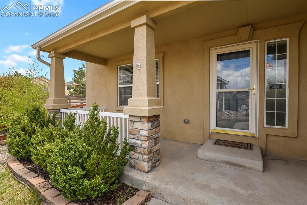 Image 4 of 48: Covered concrete front porch with stucco siding and stone-wrapped columns