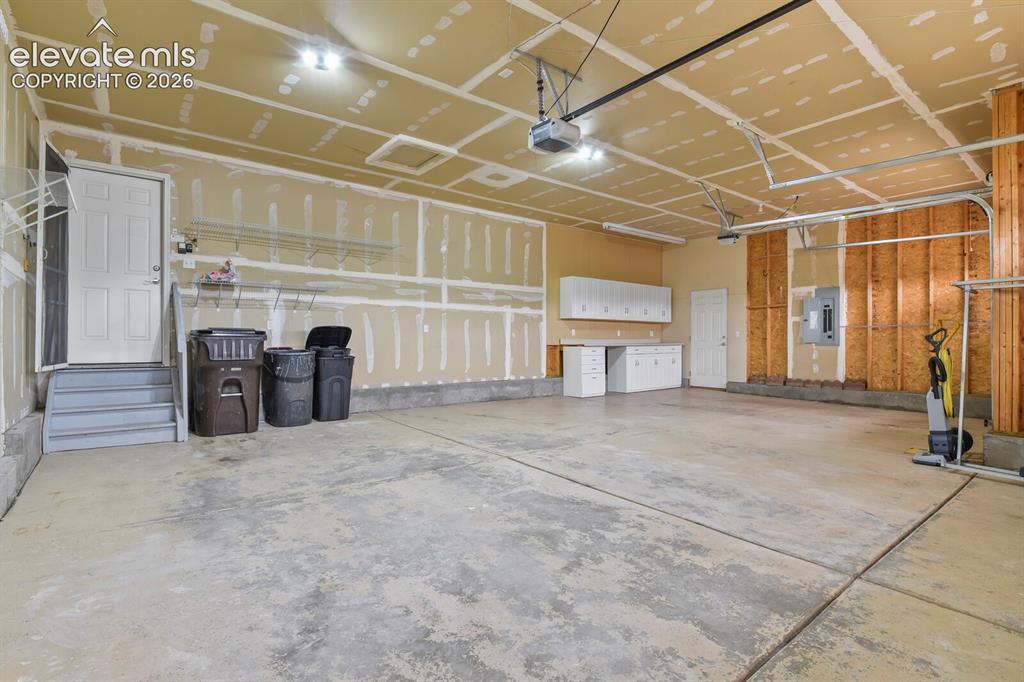 Image 43 of 48: Spacious three-car garage featuring a concrete floor, built-in cabinetry wi