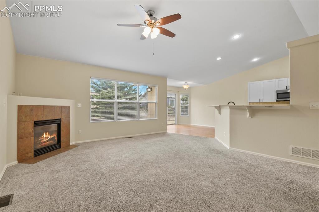Image 6 of 48: Living area featuring a tiled fireplace, large window with blinds, and a ce