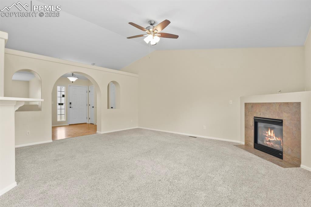 Image 9 of 43: Spacious living area featuring vaulted ceilings, a ceiling fan, plush carpe