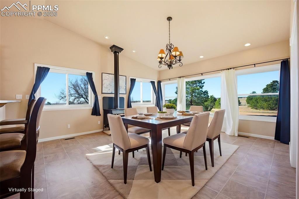 Image 10 of 50: Dining area with lofted ceiling, hanging lights, and a wood stove