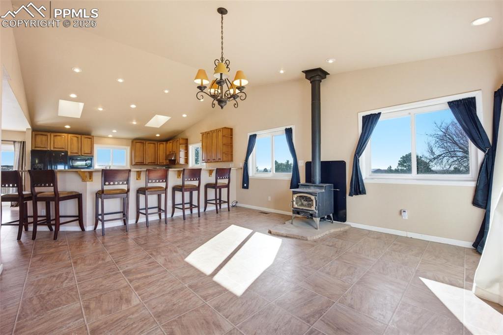 Image 8 of 50: Dining area with lofted ceiling, hanging lights, and a wood stove