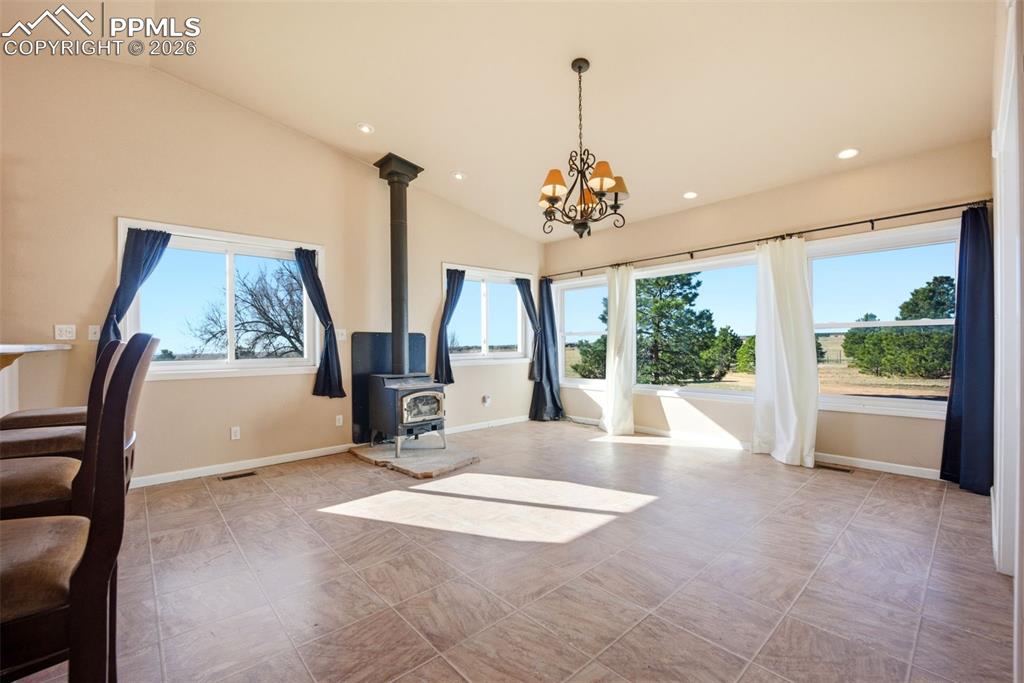 Image 9 of 50: Dining area with lofted ceiling, hanging lights, and a wood stove