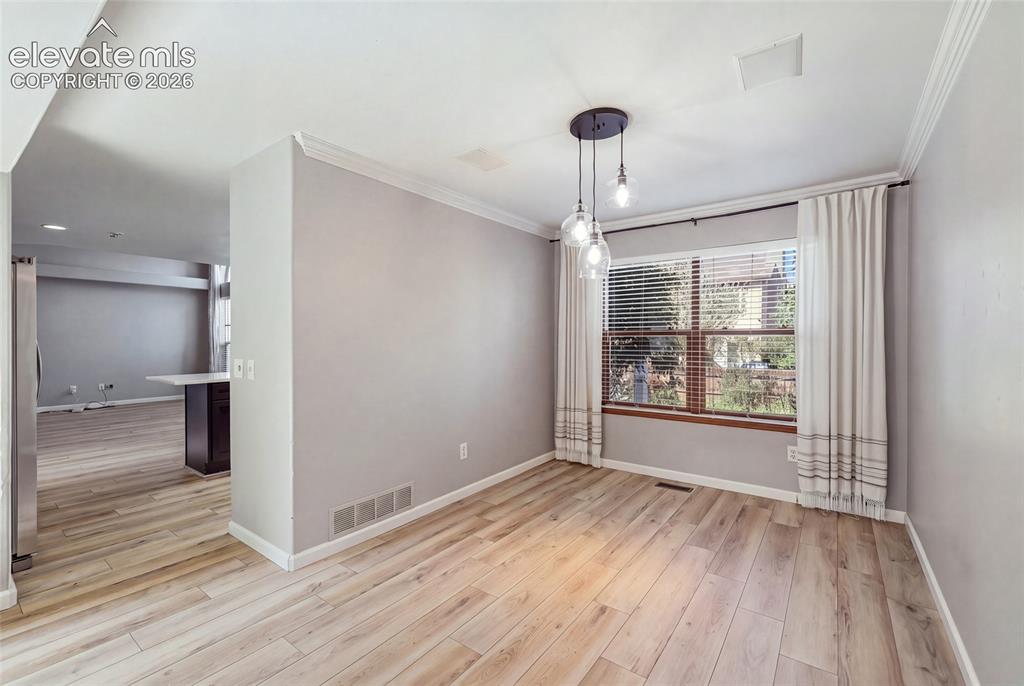 Image 10 of 50: Hardwood-style flooring, crown molding, and a modern pendant light fixture