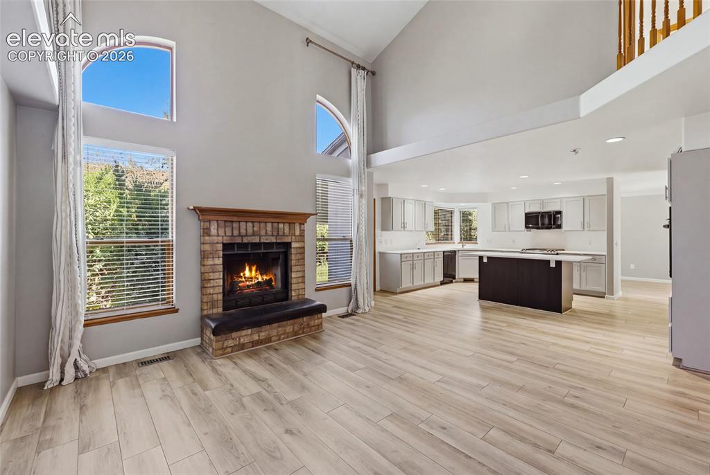 Image 19 of 50: Greatroom style, Vaulted ceiling, brick-surround fireplace with hearth, woo