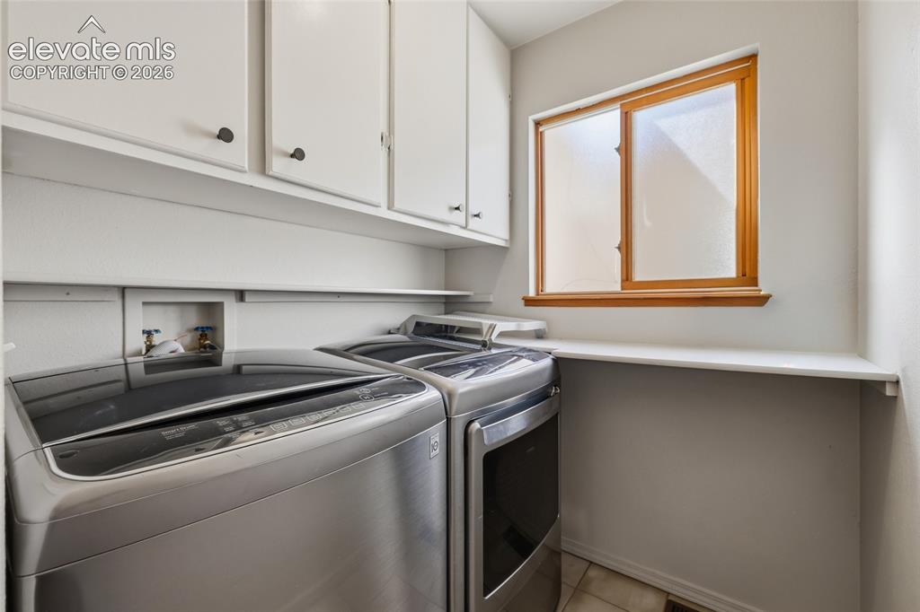 Image 21 of 50: White upper cabinetry, wood-framed window, white shelving, and tile floorin