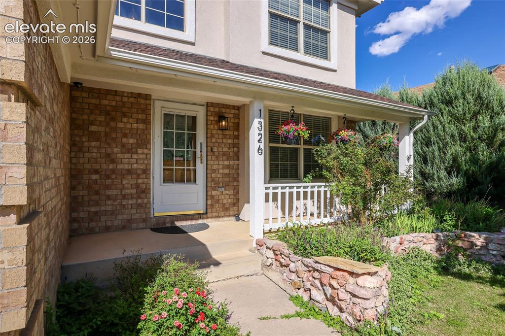 Image 3 of 50: Brick facade with a covered porch, white paneled entry door with glass inse