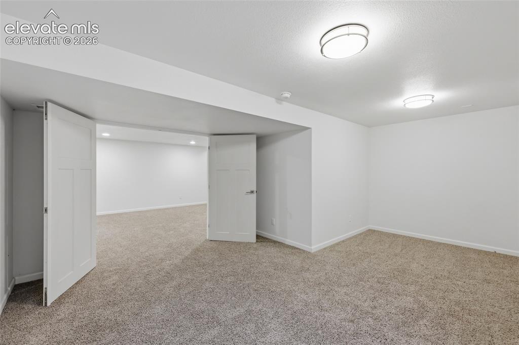 Image 39 of 50: Spacious room featuring carpeting, ceiling-mounted light fixtures, and whit