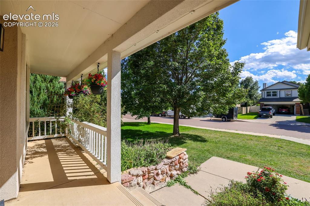 Image 4 of 50: Street view from covered front porch with white railings, concrete flooring