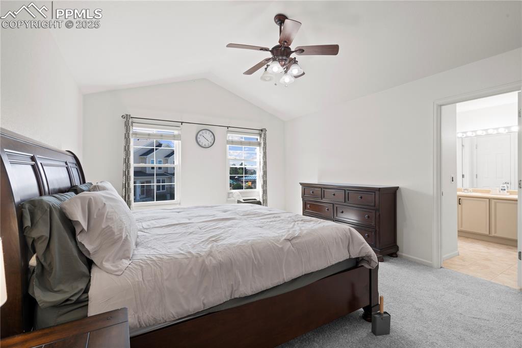 Image 22 of 29: Bedroom with lofted ceiling, light colored carpet, ensuite bath, and ceilin