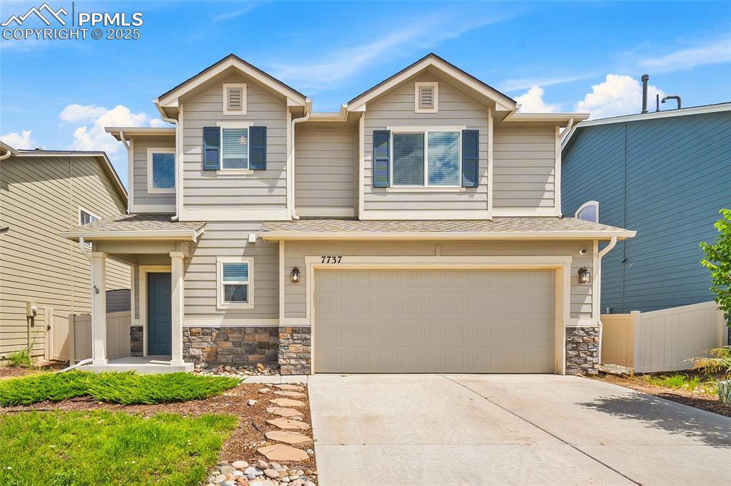 Caption: View of front of home with an attached garage, driveway, stone siding, and roof with shingles
