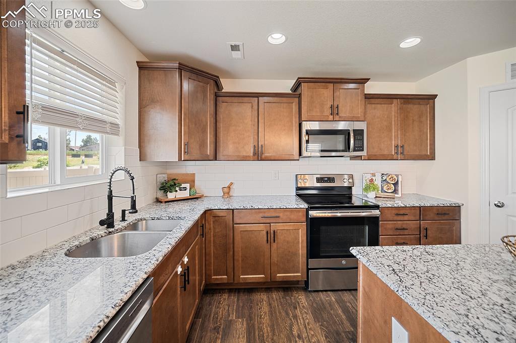 Image 17 of 50: Kitchen with stainless steel appliances, dark wood-style flooring, brown ca