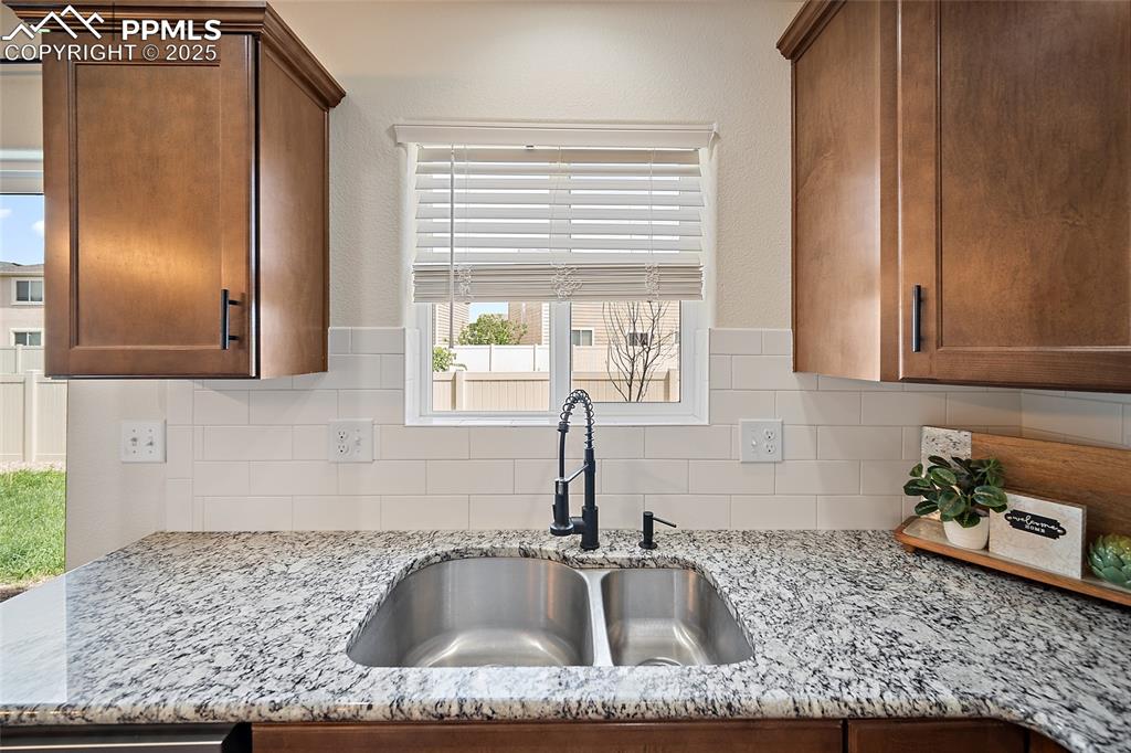 Image 18 of 50: Kitchen with decorative backsplash, light stone counters, and brown cabinet