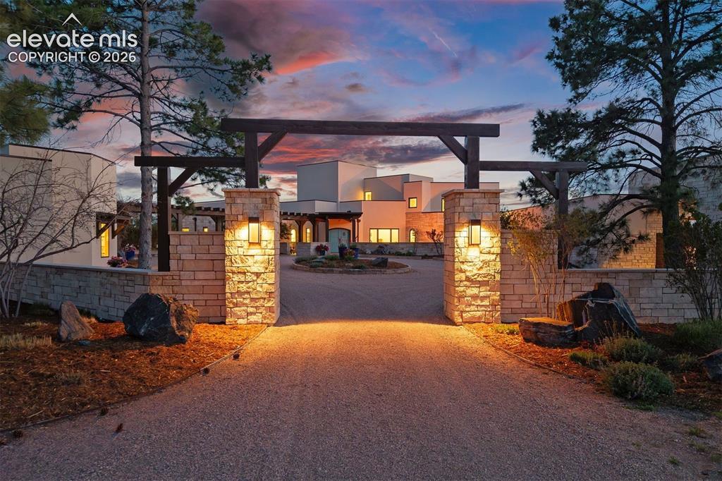 Image 9 of 46: The driveway passes through a dramatic gated entry with stacked stone pilla