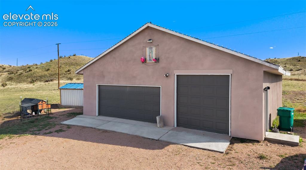 Image 29 of 34: Stucco exterior structure featuring two gray garage doors, a concrete apron