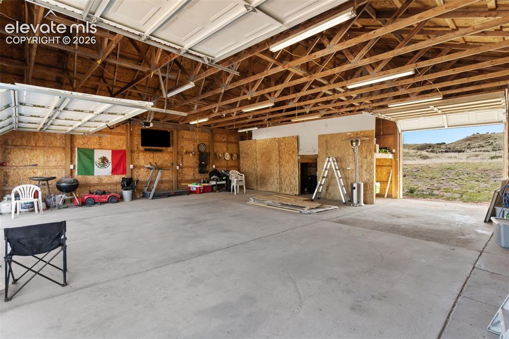 Image 30 of 34: Spacious garage featuring a concrete floor, exposed wood beam ceiling, two 