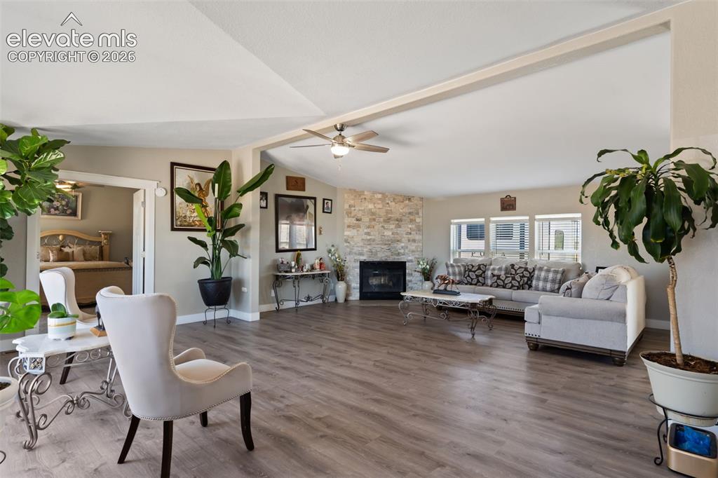 Image 8 of 34: Spacious living area featuring wood-finish flooring, a stone-clad fireplace