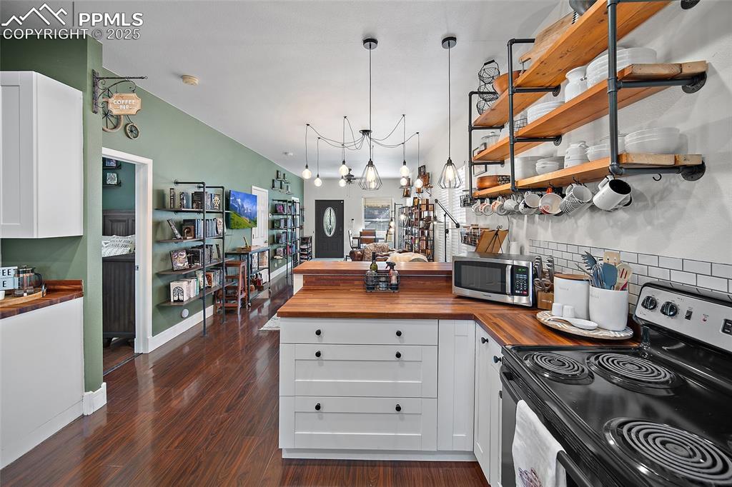 Image 13 of 36: Kitchen with wood counters, breakfast bar, backsplash and open shelving