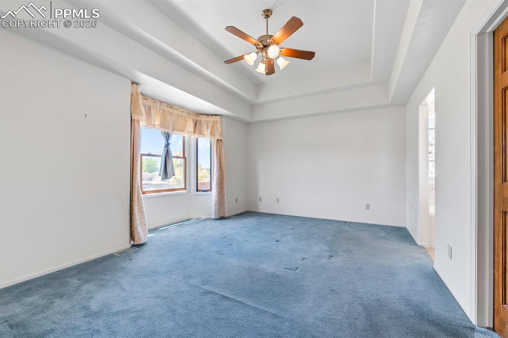 Image 12 of 38: Unfurnished room featuring a ceiling fan, carpet, and a tray ceiling