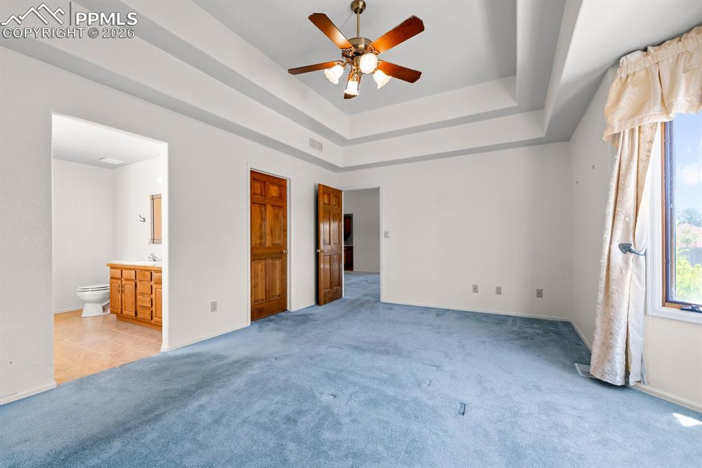 Image 13 of 38: Unfurnished bedroom featuring a tray ceiling, carpet, a ceiling fan, connec