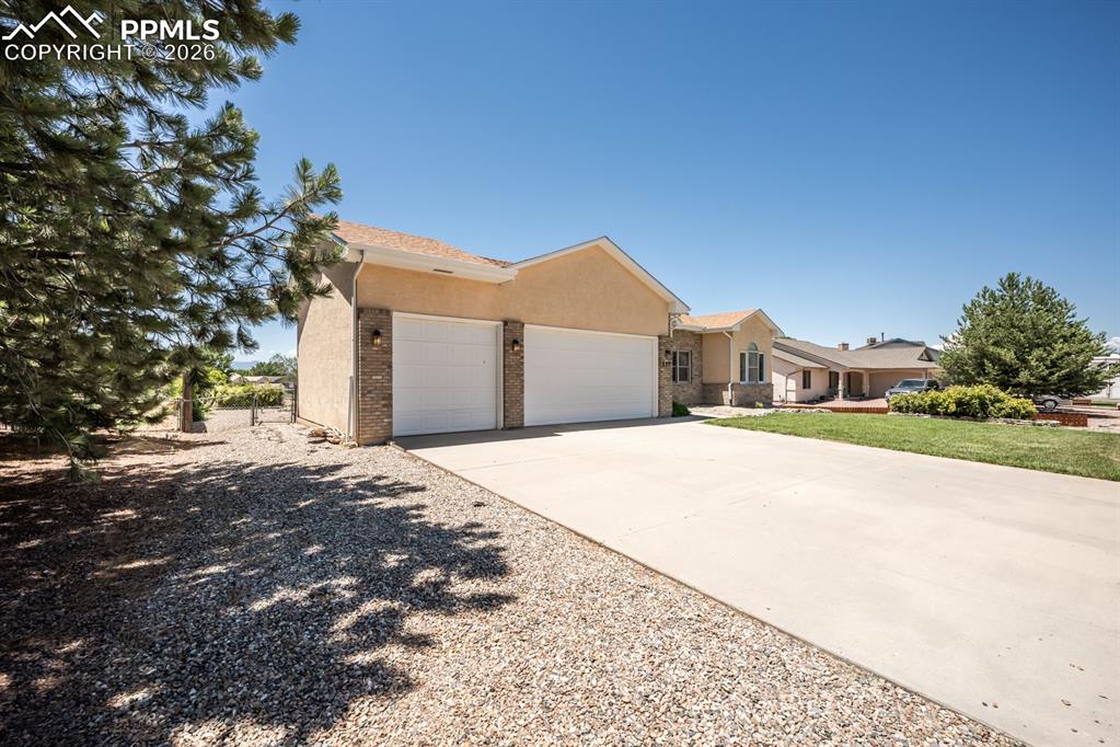 Image 2 of 38: Ranch-style house featuring a garage, driveway, stucco siding, and brick si