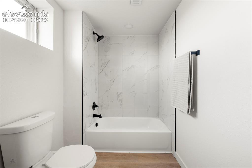 Image 39 of 49: Modern bathroom featuring a white bathtub, black fixtures, and marble-look 