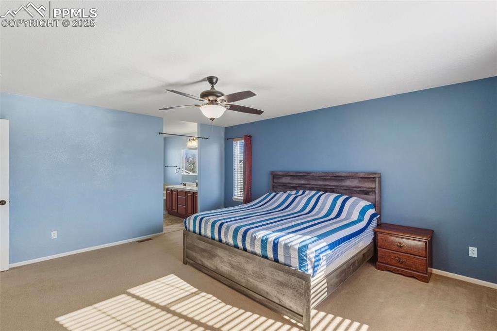 Image 15 of 33: Bedroom with ensuite bath, light colored carpet, and a ceiling fan