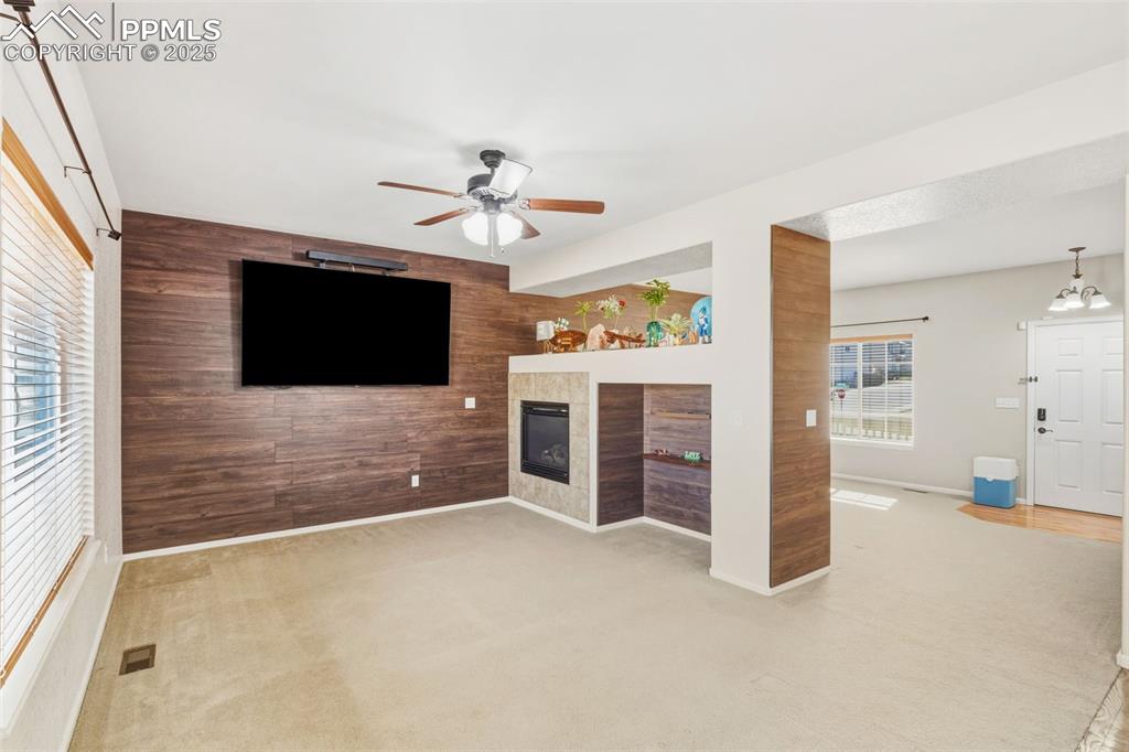 Image 4 of 33: Unfurnished living room featuring wood walls, a tiled fireplace, light colo