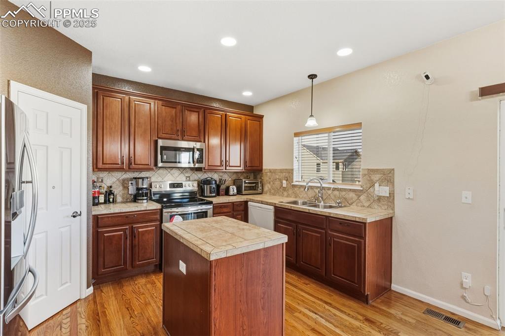 Image 7 of 33: Kitchen with a center island, hanging light fixtures, appliances with stain